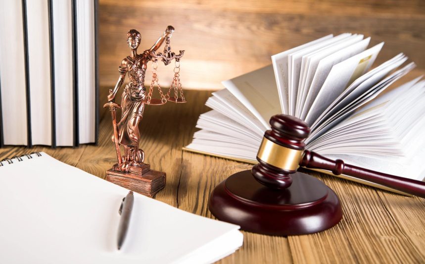 A law book, gavel and statue of justice on a table.